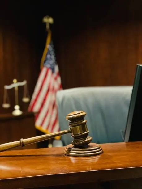 Selective focus foreground, judge’s bench, American flag and Scales of Justice defocused in background.